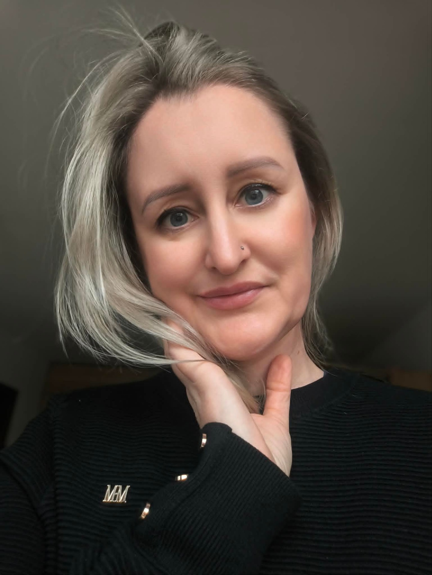 Portrét ženy s krátkými šedými vlasy, modrýma očima a jemným úsměvem, opřená o ruku. Eva Lexová zdravotní sestra piercing.